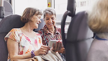 Två äldre kvinnor på buss tittar på samma mobil